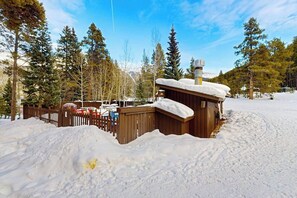 Una cabaña de madera con techo nevado, rodeada por una cerca de madera y suelo cubierto de nieve.