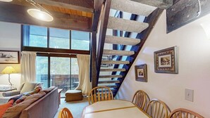 Un área de comedor con una mesa y sillas, un sofá, una escalera y cuadros en la pared.