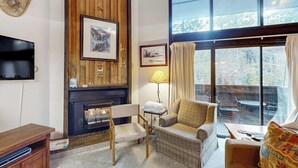 Una sala de estar acogedora con chimenea, televisor y un amplio ventanal con vistas al exterior.