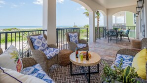 A covered outdoor seating area with wicker furniture, a round table with drinks, and a view of the beach. - Beachfront Heated Pool & Hot Tub W Mini Putt (St. Augustine)