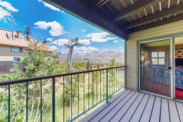 Ein Balkon mit Blick auf Berge, eine Holzterrasse und eine Glastür, die zu einem Raum mit rotem Teppich führt.