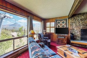 Ein Zimmer mit großem Fenster, einer Couch, einem Fernseher und einem Kamin.