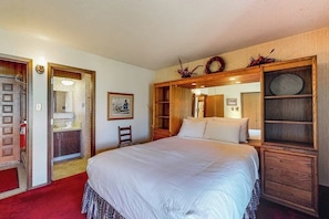 Ein Schlafzimmer mit einem großen Bett, einem Holz-Kopfteil, einem kleinen Stuhl und einem Spiegel.