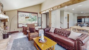 Een ruime woonkamer met een leren bank, een houten salontafel en een stenen openhaard.