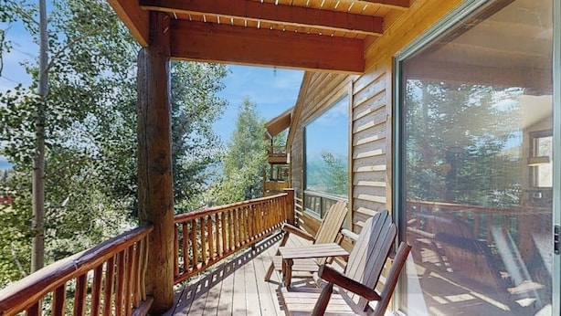 Een houten terras met stoelen en een glazen balustrade met uitzicht op een bebost gebied.