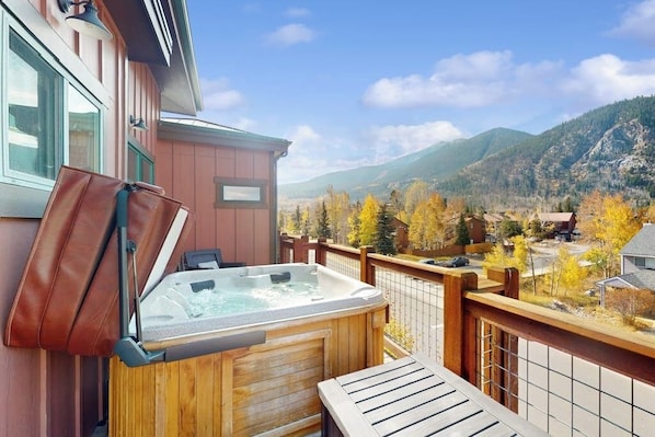 Eine Holzterrasse mit Whirlpool, einem Sessel und Blick auf Berge und Herbstbäume.