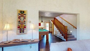 A room with a pool table, a wooden staircase, and a wall with a tapestry.