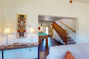 Una habitación con mesa de billar, una escalera de madera y un tapiz en la pared.