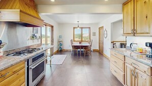 A kitchen with wooden cabinets, a dining area with a table and chairs, and a view through a window.