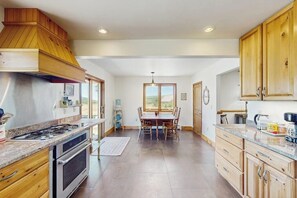Una cocina con armarios de madera, un comedor con mesa y sillas, y vistas por una ventana.