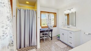 A bathroom with a shower curtain, a window, a sink, and a mirror.
