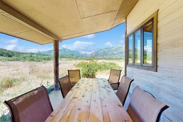 Una mesa de madera con sillas bajo un porche cubierto, con vista a un paisaje natural.