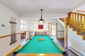 A pool table in a room with a wooden staircase and a door leading to another room.