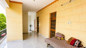 A room with a bed, a bench, a fan, and a door leading to another room.