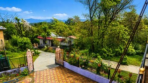 A residential area with a paved walkway leading to a gated entrance, surrounded by lush greenery and a distant mountain view.