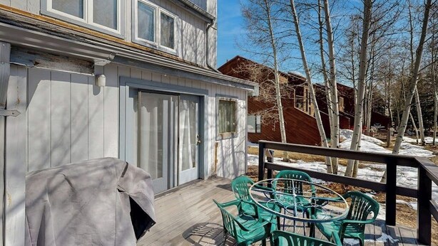 Une terrasse en bois avec des chaises vertes et un barbecue.