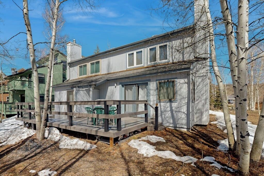 A two-story house with a deck, surrounded by trees and snow patches.