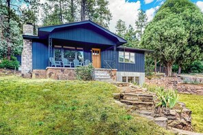 A two-story house with a stone foundation, a front porch with chairs, and a stone staircase leading to the entrance. - Upper apartment with deluxe kitchen, private W/D, & great location (Durango)