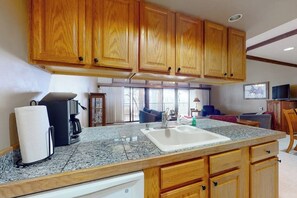 Una cocina con armarios de madera, encimera de granito, cafetera y lavabo.