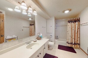 Un baño con un espejo grande, un lavamanos, un inodoro y una zona de ducha.