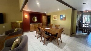 Ein Essbereich mit Holztisch und -stühlen, im Hintergrund eine Küche und eine Treppe, die zu einer oberen Ebene führt.