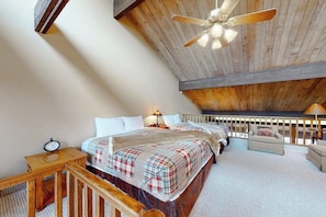 Ein Schlafzimmer mit Holzboden, einem Bett mit Karoüberwurf, einem Nachttisch mit einer Uhr und einem Holzbalken.