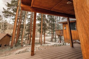 A wooden deck with a view of tall pine trees and a cabin. - Riverfront Hot Tub Mountain Retreat (Grand Lake)