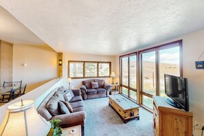 Ein Wohnzimmer mit einer Couch, einem Couchtisch, einem Fernseher und großen Fenstern.