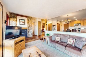 Ein Wohnzimmer mit Fernseher, Sofa, Couchtisch und einer Küche im Hintergrund.