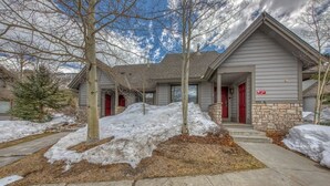 A residential house with a stone foundation, red doors, and a snow-covered yard. - Spacious resort home w/private garage, hot tub & laundry. Bus to slope (Copper Mountain)