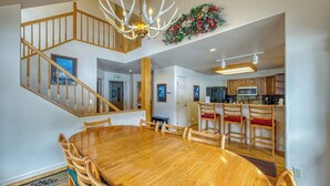 A dining area with a wooden table and chairs, a staircase, and a kitchen in the background. - Spacious resort home w/private garage, hot tub & laundry. Bus to slope (Copper Mountain)