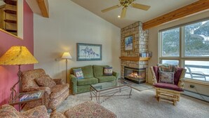 A cozy living room with a fireplace, a ceiling fan, and a large window. - Spacious resort home w/private garage, hot tub & laundry. Bus to slope (Copper Mountain)