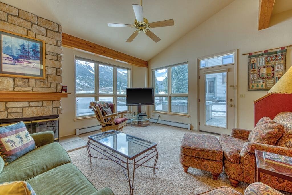 A living room with a stone fireplace, a television, and a large window.