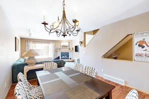 A dining area with a chandelier, patterned chairs, a wooden table, and a sofa.