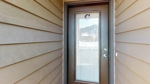Une porte dotée d’une poignée en métal et d’un panneau en verre, intégrée à un bâtiment dont le revêtement extérieur est de couleur beige.