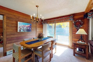 Ein Holzinterieur mit Esstisch, Stühlen, einer Deckenleuchte, einem Fenster mit Aussicht und einem kleinen Tisch mit Lampe.