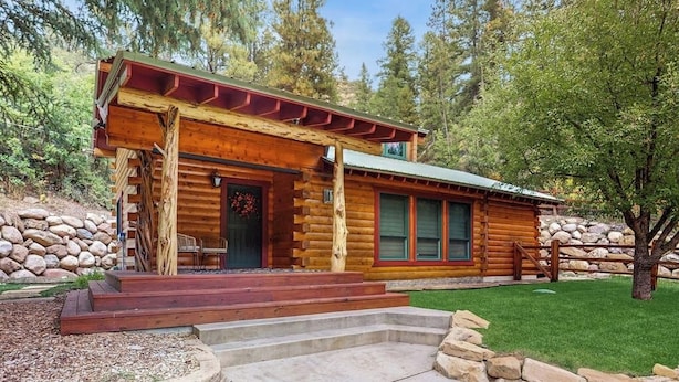 A log cabin with a porch, stone wall, and a well-maintained lawn. - Mountain home with gas fireplace, dog-friendly and outdoor deck with BBQ (Durango)