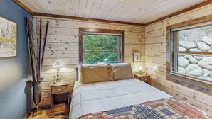 A wooden cabin bedroom with a bed, a window with a view of rocks, a nightstand with a lamp, and a wall-mounted picture. - Mountain home with gas fireplace, dog-friendly and outdoor deck with BBQ (Durango)