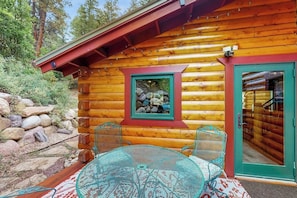 Eine Blockhütte mit Glastür, einem kleinen Fenster mit Blick auf Felsen und einem runden Tisch mit Stühlen draußen.