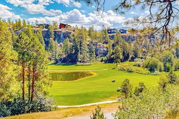 Ein Golfplatz mit Teich, umgeben von Bäumen und einer felsigen Klippe.