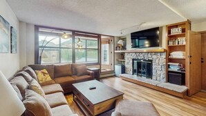 Een woonkamer met een stenen openhaard, een groot raam en een bank.