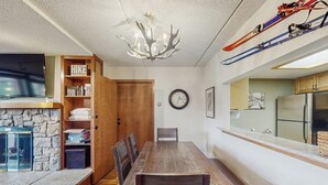 Een eetruimte met een houten tafel en stoelen, een stenen openhaard, een klok en ski's die aan de muur hangen.