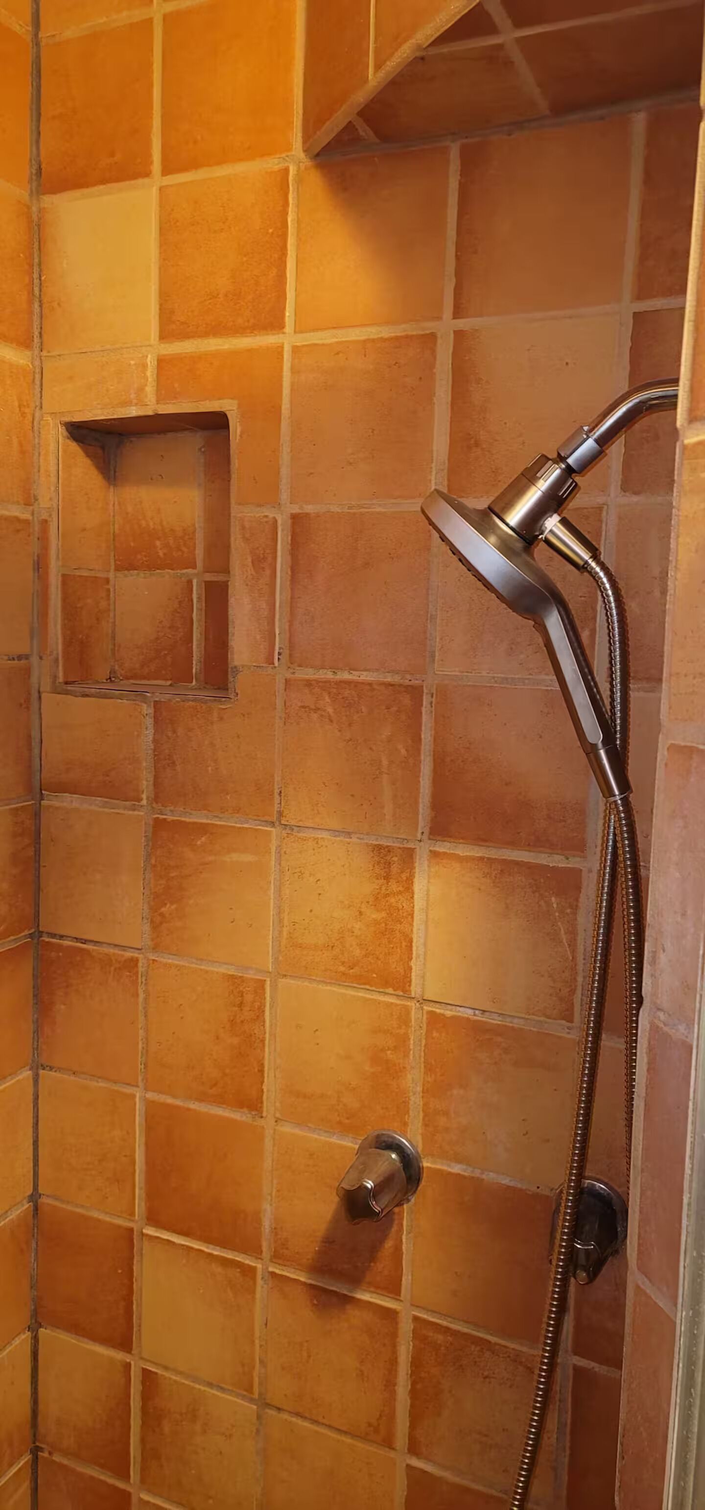 A shower with a handheld showerhead and a wall-mounted control valve.