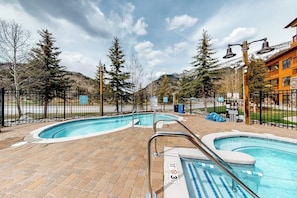 Ein Pool mit Backstein-Terrasse, umgeben von einem Zaun, und ein Gebäude mit Holzfassade im Hintergrund.