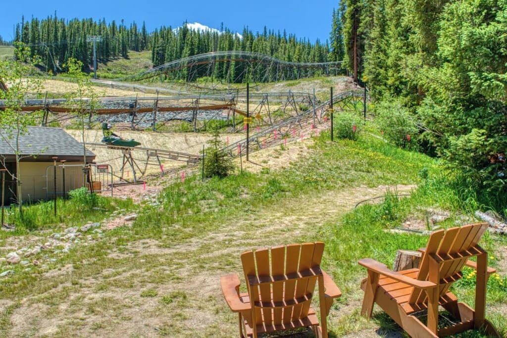 A wooden chair in a grassy area with a view of a railway track and forest.