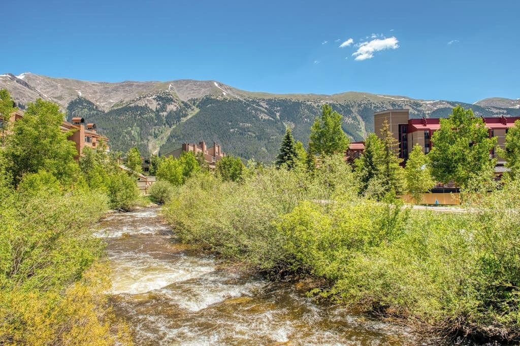 Une rivière traverse une vallée, avec des bâtiments situés sur la rive droite, le tout étant entouré de verdure et avec des montagnes en arrière-plan.