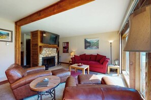 Ein Wohnzimmer mit Kamin aus Stein, Ledersofas, einem roten Sofa und einem Fernseher.