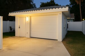 Eine Garage mit geschlossener Tür, eine kleine Veranda mit einer Lampe und ein weißer Zaun.