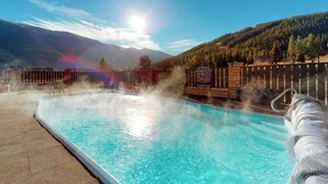 Una piscina con vapor saliendo del agua, rodeada de montañas y una cerca de madera.