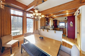 A dining area with a wooden table and benches, a chandelier, and a view of the outdoors through large windows. - Well-appointed home with home theater, radiant heat & private hot tub (Fraser)